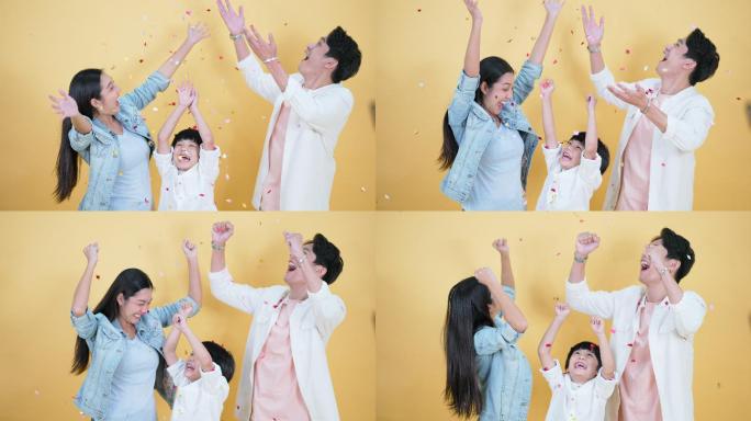 年轻的亚洲家庭母亲父亲和儿子一起玩耍。庆祝，并在他们身上洒上丝带，双手高兴地跳起来。惊讶、兴奋、开心