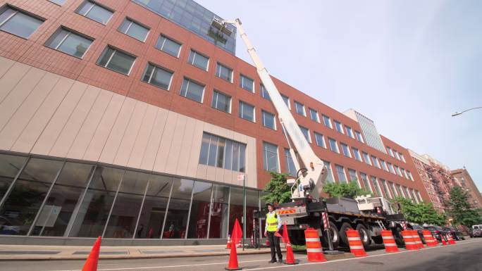 纽约市哈莱姆街上，一名身穿黄色安全背心的体力劳动者在工地上管理交通。