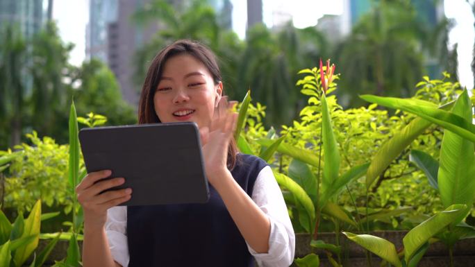 年轻的亚洲女商人在城市的一个室外公园使用数字平板电脑进行视频通话