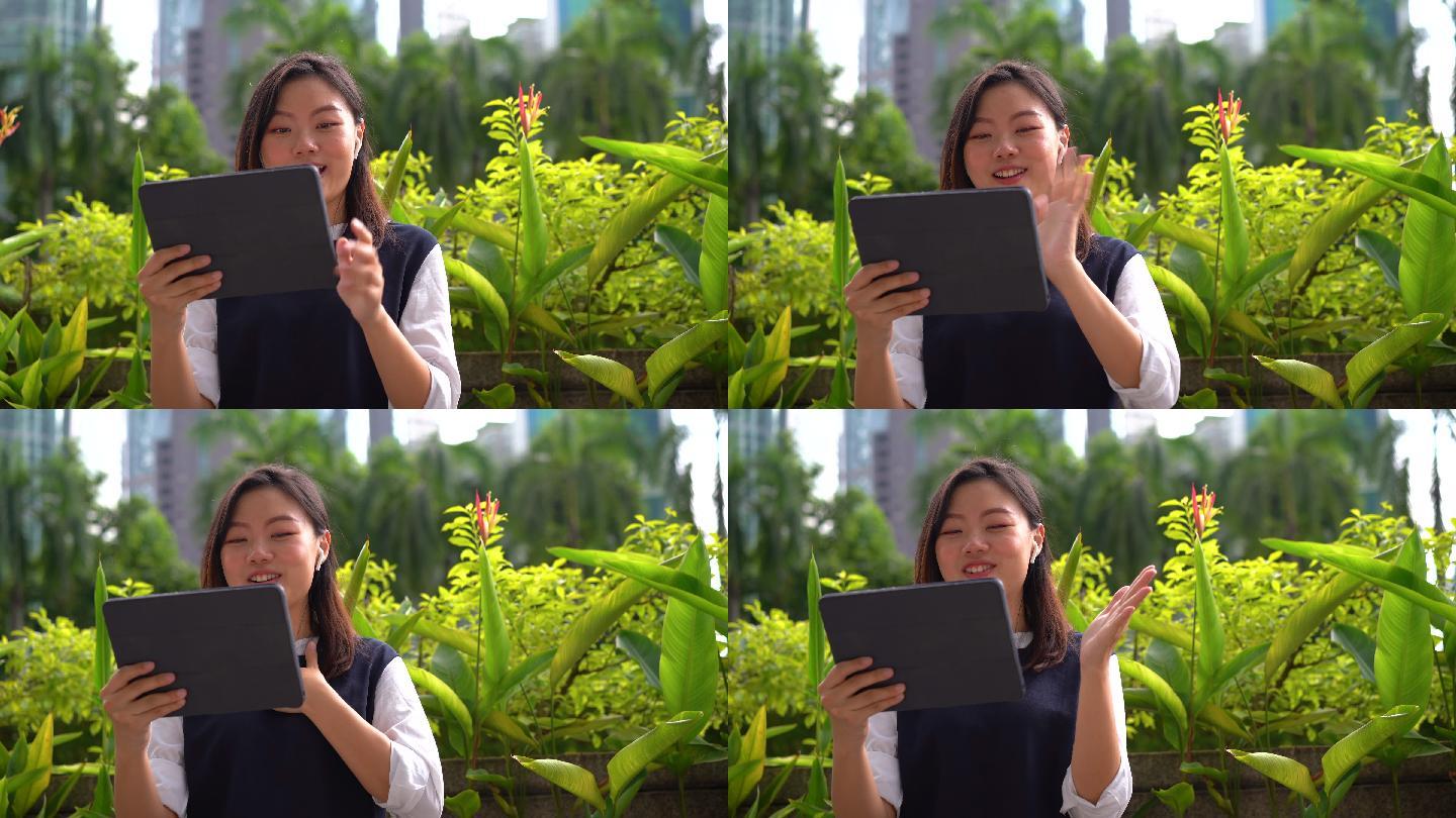 年轻的亚洲女商人在城市的一个室外公园使用数字平板电脑进行视频通话