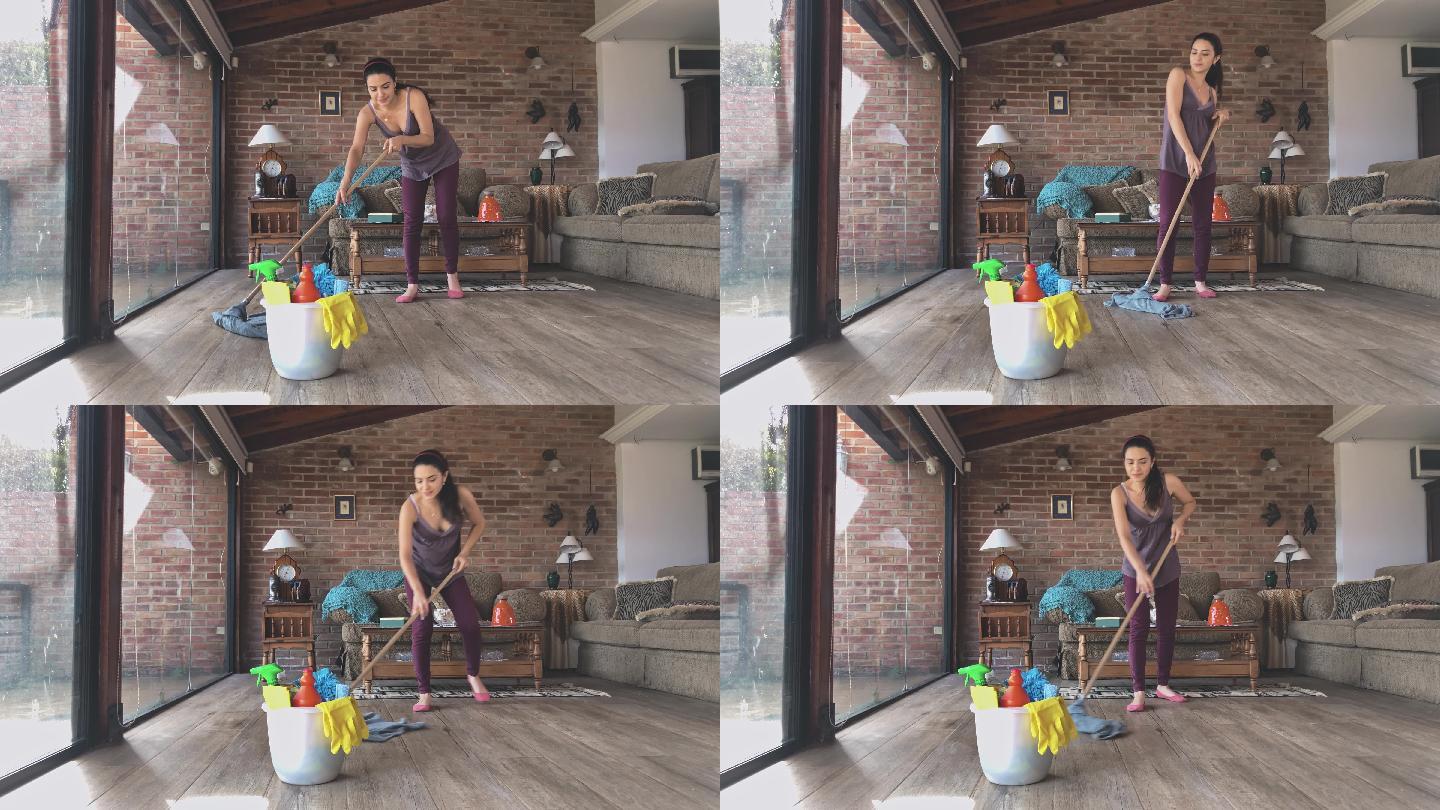 一名西班牙裔年轻女子在客厅用拖把和装有清洁用品的塑料桶清洁硬木地板