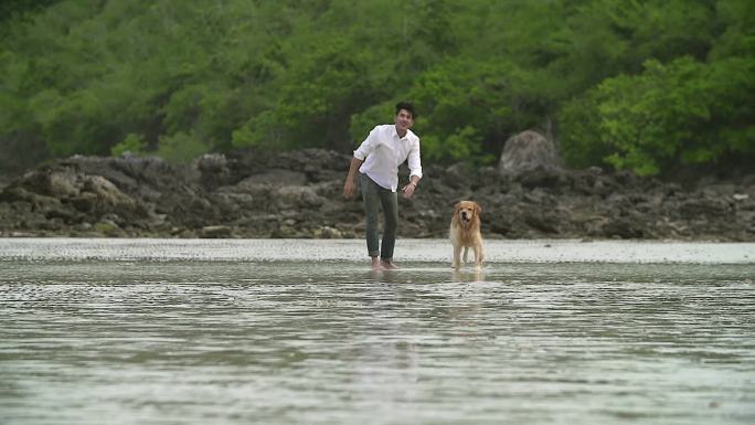 高清慢镜头：年轻人在海滩上和他的狗玩耍。