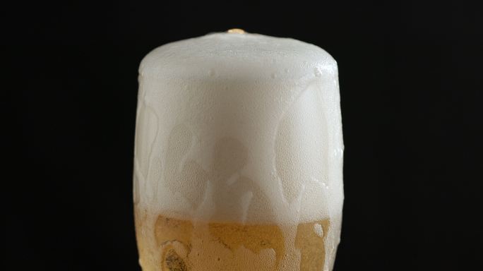 啤酒倒入玻璃杯中，沿边缘倒入，然后沿玻璃杯侧面流动