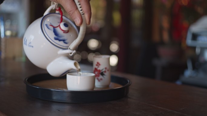 在咖啡馆里，女人用手把茶倒进白色陶瓷杯里，慢镜头