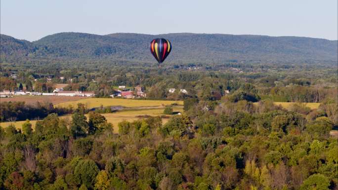初秋的一个阳光明媚的夜晚，热气球正飞越美国宾夕法尼亚州波科诺斯的利海山谷。具有向后平移电影摄影机运动