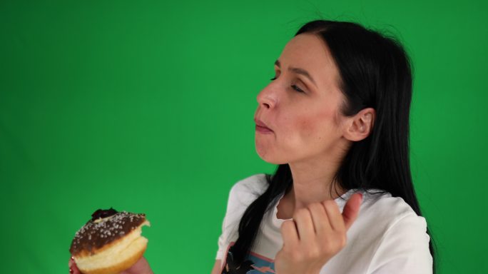 在绿色背景前吃巧克力甜甜圈时，这位女士用鬼脸来表达她对味道的想法