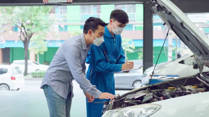 亚洲汽车技师听取客户解释汽车状况。新冠疫情期间，车辆服务经理戴口罩，在机械车间维护和修理车库中的汽车