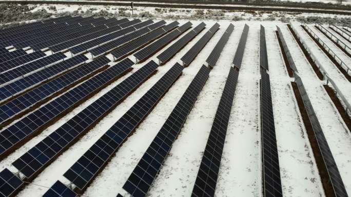 4k无人机拍摄的多排太阳能电池板农场在冬季公路附近的雪地中创造太阳能