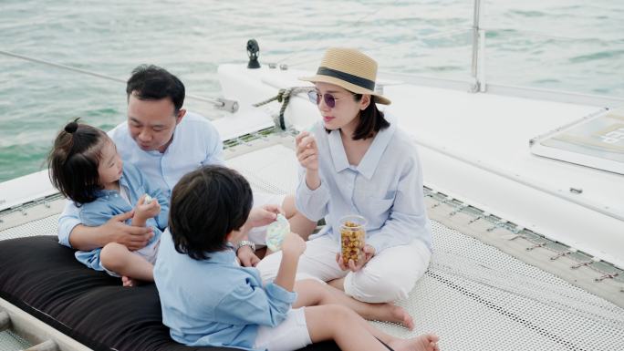 幸福的一家人一起坐在漂浮在海上的豪华游艇上野餐。一家人在帆船上吃零食。他们在吃饼干，聊天，享受新鲜空
