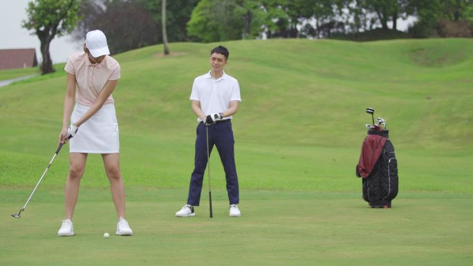 中国亚裔成熟女子高尔夫球手在高尔夫球场边打高尔夫球边看朋友