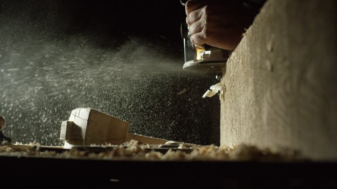 一名白人木工在红橡木板边缘使用刨刀，锯屑喷洒在工作台和自制木槌上