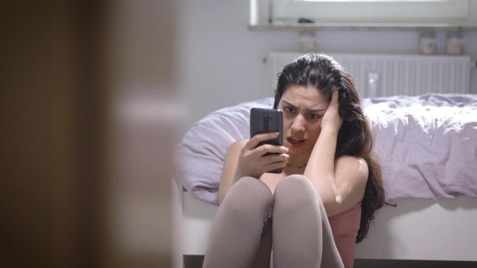 坐在床边使用智能手机的悲伤女人