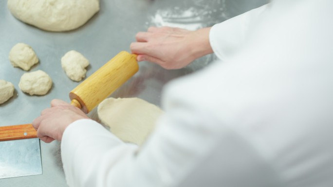 俯视图：厨师在成型前揉捏和滚动面团，添加一些面粉以减少粘性，准备面团，在商业烘焙厨房制作面包和馒头