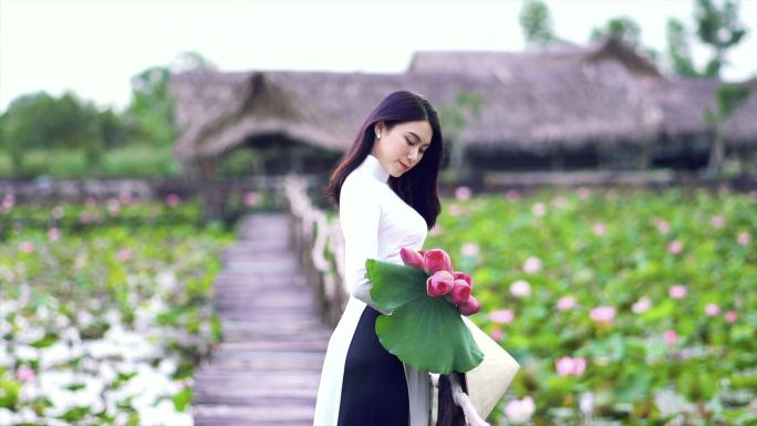 4K慢镜头FHD画面，美丽的越南女子手持粉红莲花，微笑在大莲湖木桥上，越南，亚洲或东南亚旅游概念