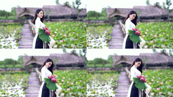 4K慢镜头FHD画面，美丽的越南女子手持粉红莲花，微笑在大莲湖木桥上，越南，亚洲或东南亚旅游概念
