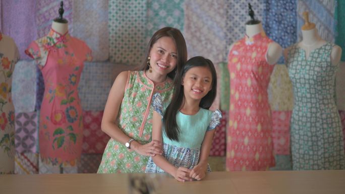 马来西亚华裔美丽的母女肖像在她的蜡染旗袍面料纺织品收藏零售店前微笑着看着相机