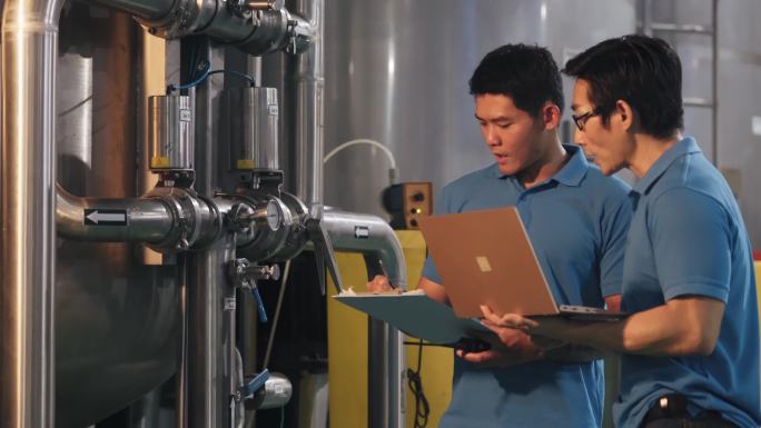 2名亚裔中国技师维护工程师记录水箱中的压力计读数瓶装水厂的日常质量控制在剪贴板上书写进度