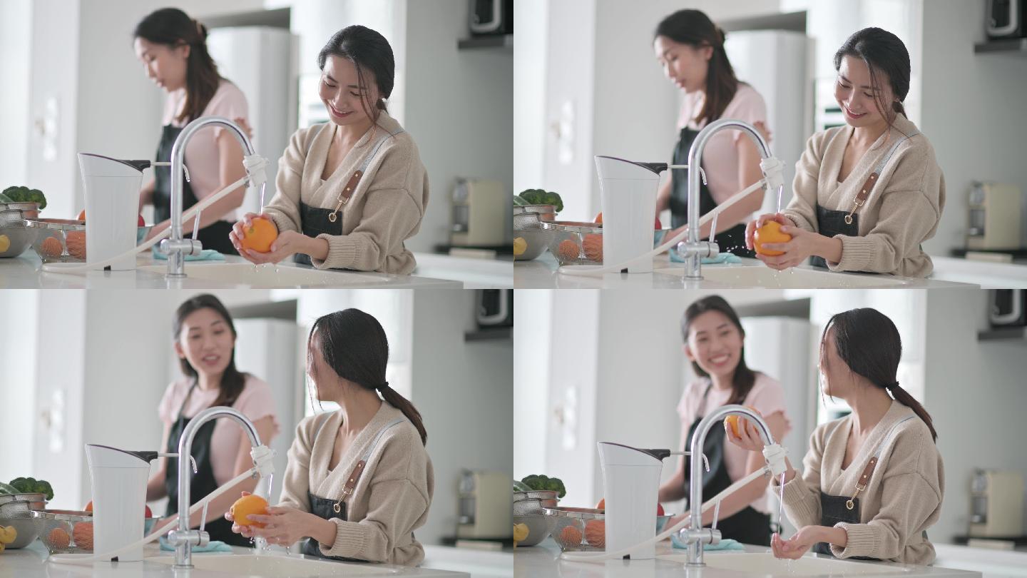 周末，亚裔中国女性在家中用笔记本电脑在厨房柜台用自来水清洗水槽中的橙色水果