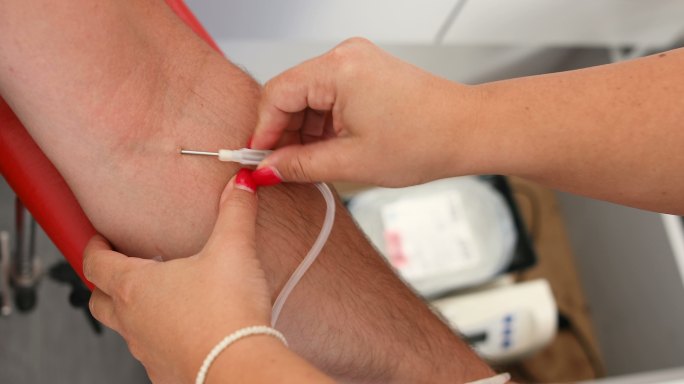 护士将医用针头刺入捐献者的手臂。善行。为你的身体献血的好处。接受输血者的手。临床献血者的特写镜头