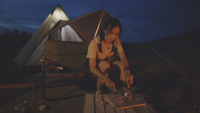 泰国清迈，年轻女性在黑暗中篝火露营时制作牛排