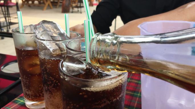 将可乐/可乐/苏打水倒入桌子上的玻璃杯中