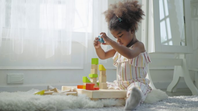 非洲女儿在客厅里玩积木玩具堆得最高，高兴地躺在地毯上，笑着，笑着。学前概念，低角度视图。