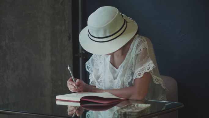 戴着白色帽子、穿着复古白色连衣裙的亚洲艺术家正在为周末旅行的休闲活动写作和素描
