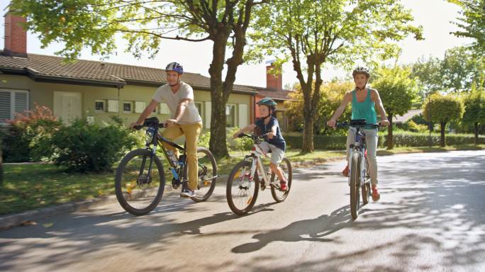 阳光明媚的日子里，DS父母和他们的儿子在一个不错的社区骑自行车