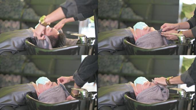 男美发师在美发沙龙洗完头发后，用毛巾把亚裔中国男性顾客裹起来