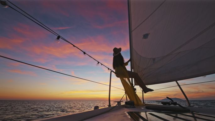 落日时分，身着黄色长裙的斯洛莫女子在帆船船头享受微风