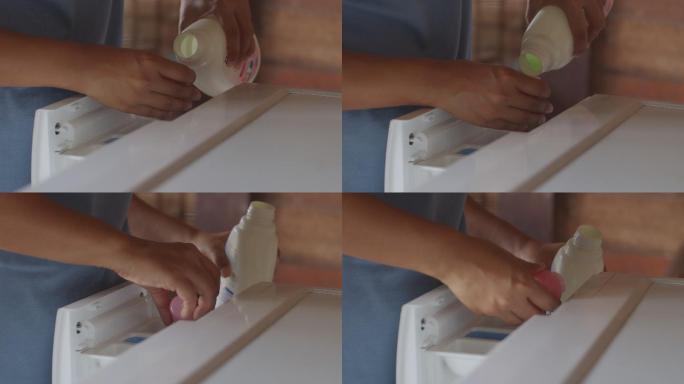 做家务的亚洲女人。女人用手将液体软化剂倒入洗衣机，在家里洗衣服。