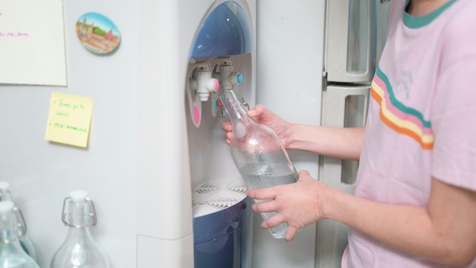女人在家里用玻璃瓶装水净水器