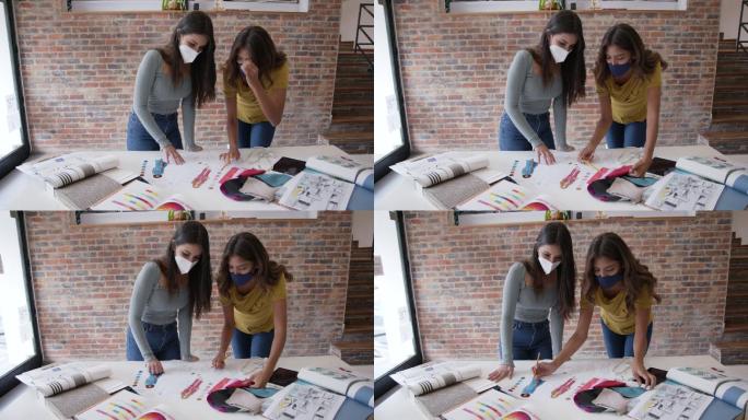 拉丁美洲女性设计师团队正在开发一个新系列，查看草图并选择面料，两者都戴着防护面罩