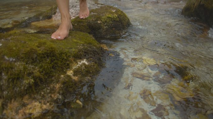 一个女人踩在河里的岩石上的慢腾腾的脚