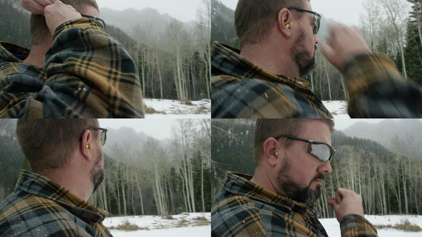 一位30多岁留着胡子的白种人在山里雪天的树林里把耳塞塞进耳朵里