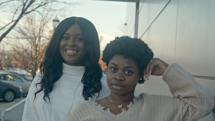 两位年轻貌美的非裔美国/海地女性朋友在市中心摆姿势进行精彩对话