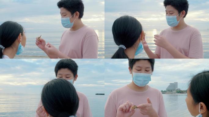 日出时分，一个戴着面具的亚洲男孩在海滩上用手抓寄居蟹。男孩告诉他的妹妹关于寄居蟹的生活理念。