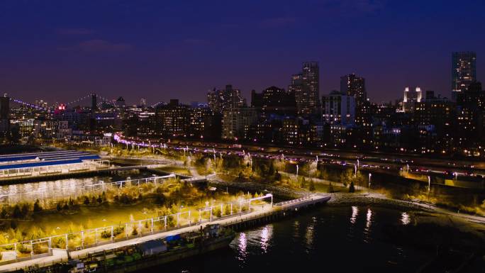 夜景中布鲁克林大桥公园、码头和BKE上的交通鸟瞰图，背景是照亮的布鲁克林。无人机利用宽全景轨道相机运