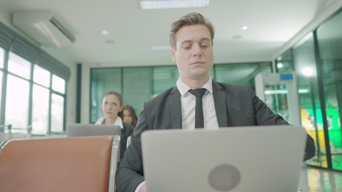 一位白人高管，一位坐在笔记本电脑上工作的商人，在机场候机室看着时钟，准备和其他乘客一起登机。商务人士