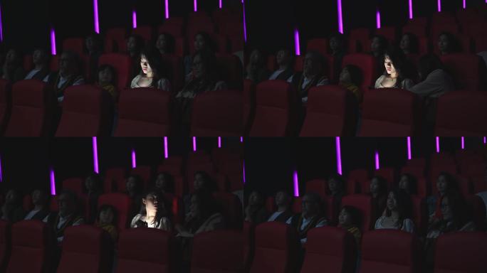 一名亚裔中国女性在电影放映期间，在黑暗中阅读手机短信，忽视并干扰周围的其他观众
