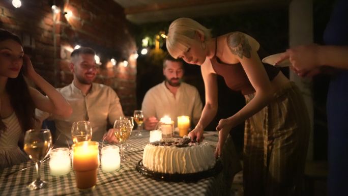 一个女人在切生日蛋糕，而她的女性朋友在帮她