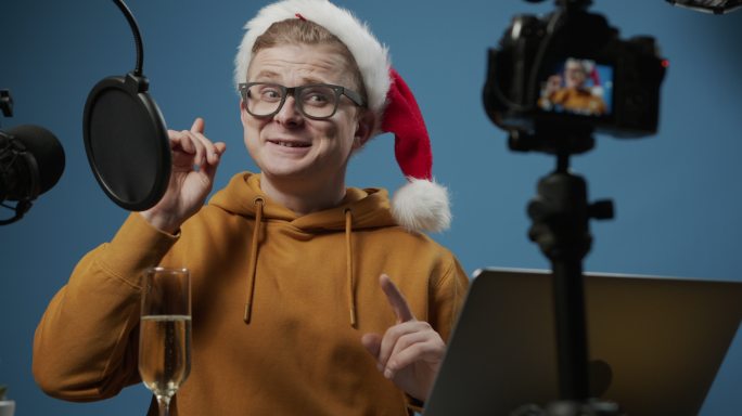 一段背景特写视频，一位年轻迷人的视频博主戴着圣诞帽，一边喝着香槟，一边愉快地谈论假期，