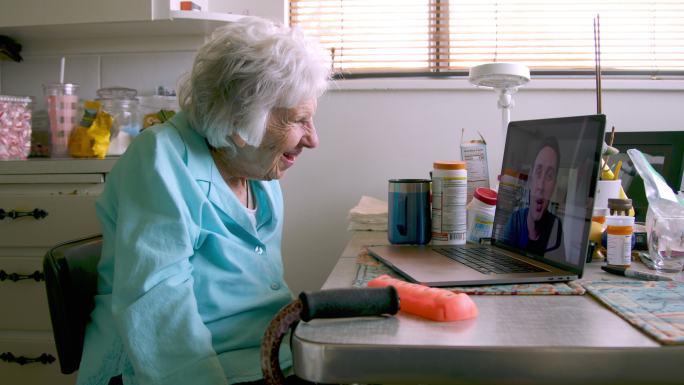 一位100岁的老妇人坐在笔记本电脑前与孙子交谈并打视频电话
