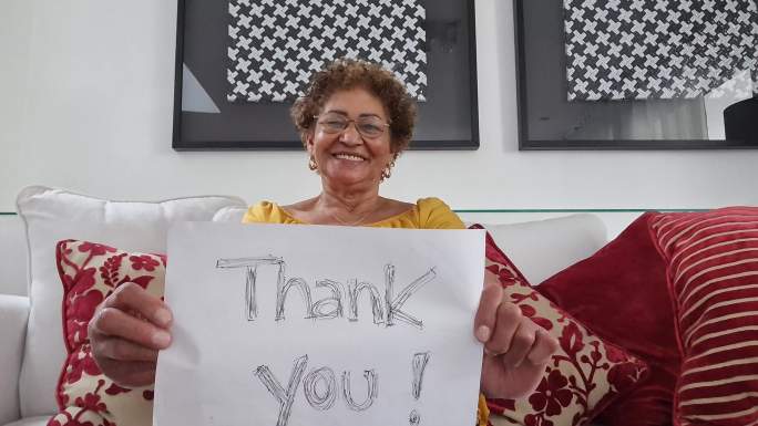 资深女士在视频通话中展示写有“谢谢”的论文-网络摄像头视角