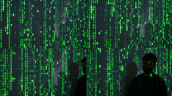 一名男性黑客在电脑上工作，而绿色代码字符则映照在他的脸上