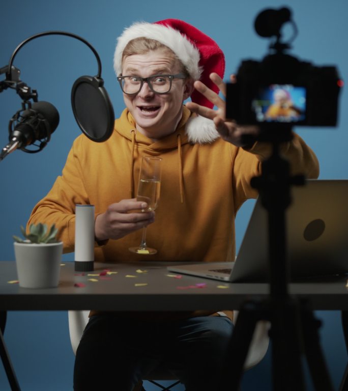 一位年轻可爱的博主在蓝色背景的工作室里用饼干和香槟为他的频道拍摄圣诞场景