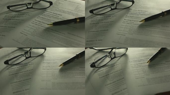 用钢笔、眼镜在办公桌上平移简历照片。