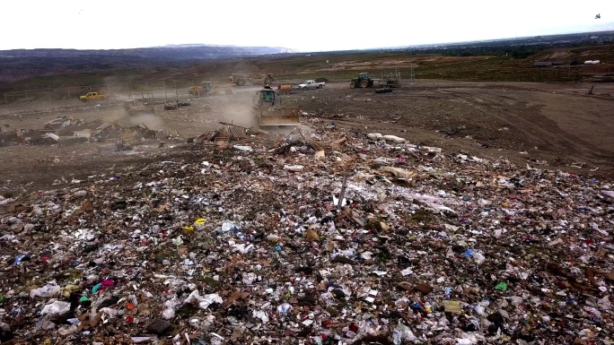 一个商业垃圾填埋场的空中无人机视角，拖拉机正在刮垃圾