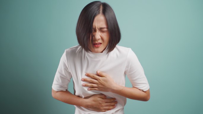 一名亚洲女子胃痛，孤零零地站在蓝色背景上。4K视频。医疗保健概念。
