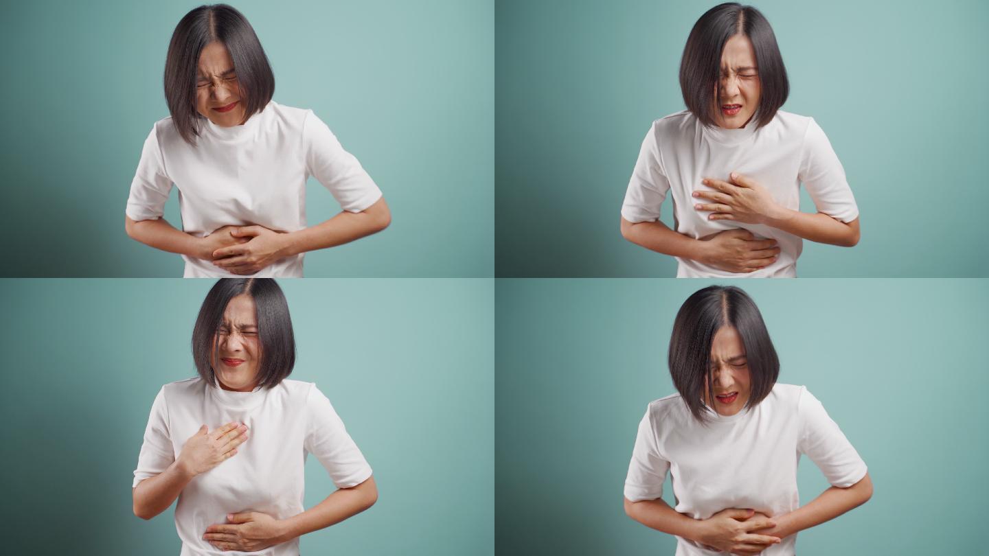 一名亚洲女子胃痛，孤零零地站在蓝色背景上。4K视频。医疗保健概念。